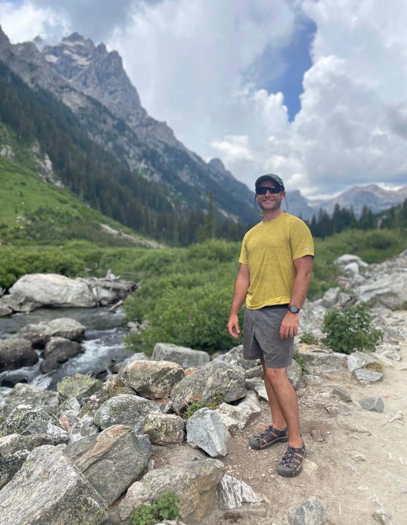 white man wearing a ball cap and sunglasses with a mountain landscape behind him