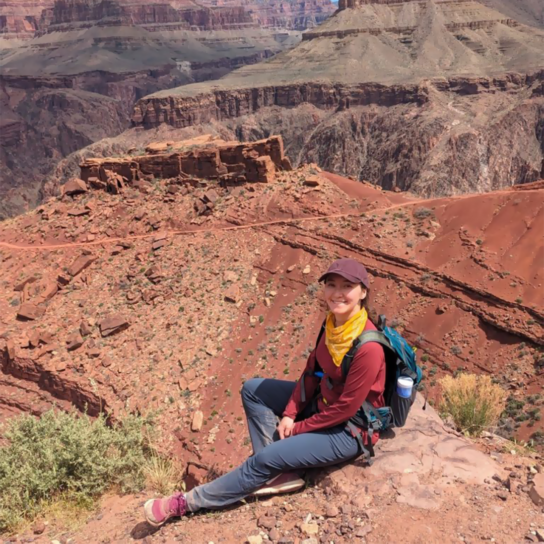 woman wearing hiking gear and a ball cap sitting with orange cliffs in the background