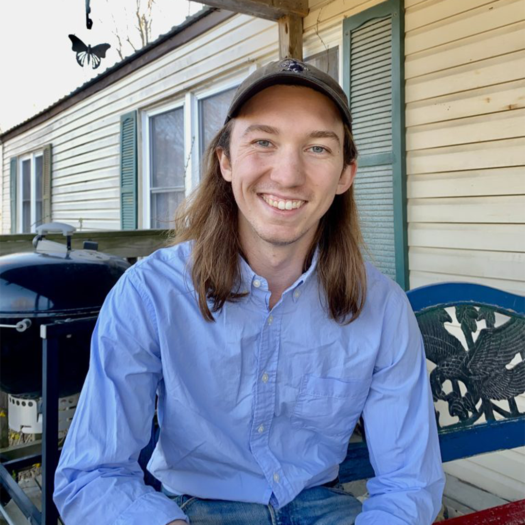 headshot of a white man with long light brown hair and a ball cap