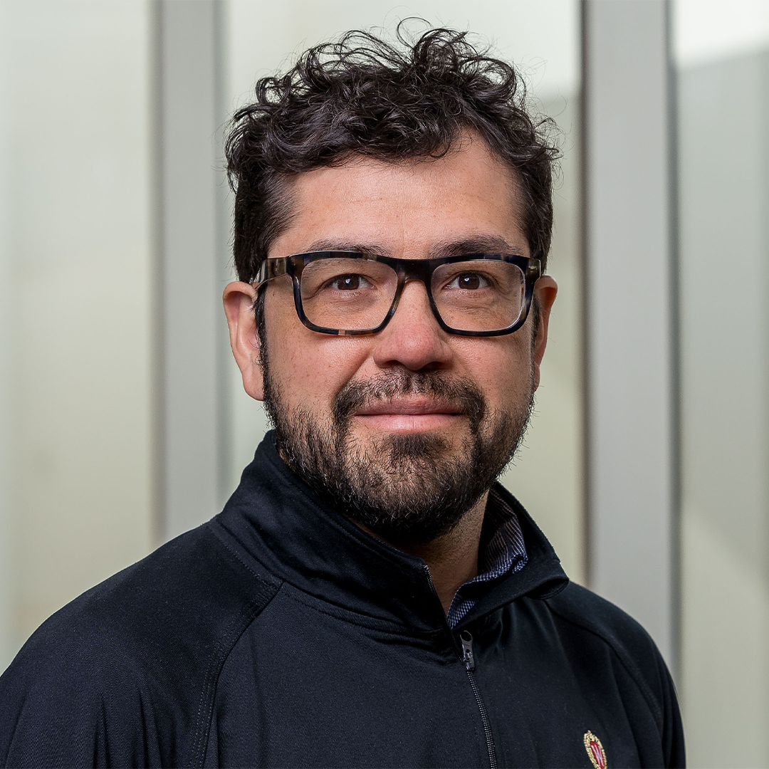 headshot of man with light brown skin, dark brown hair, a short beard, and glasses