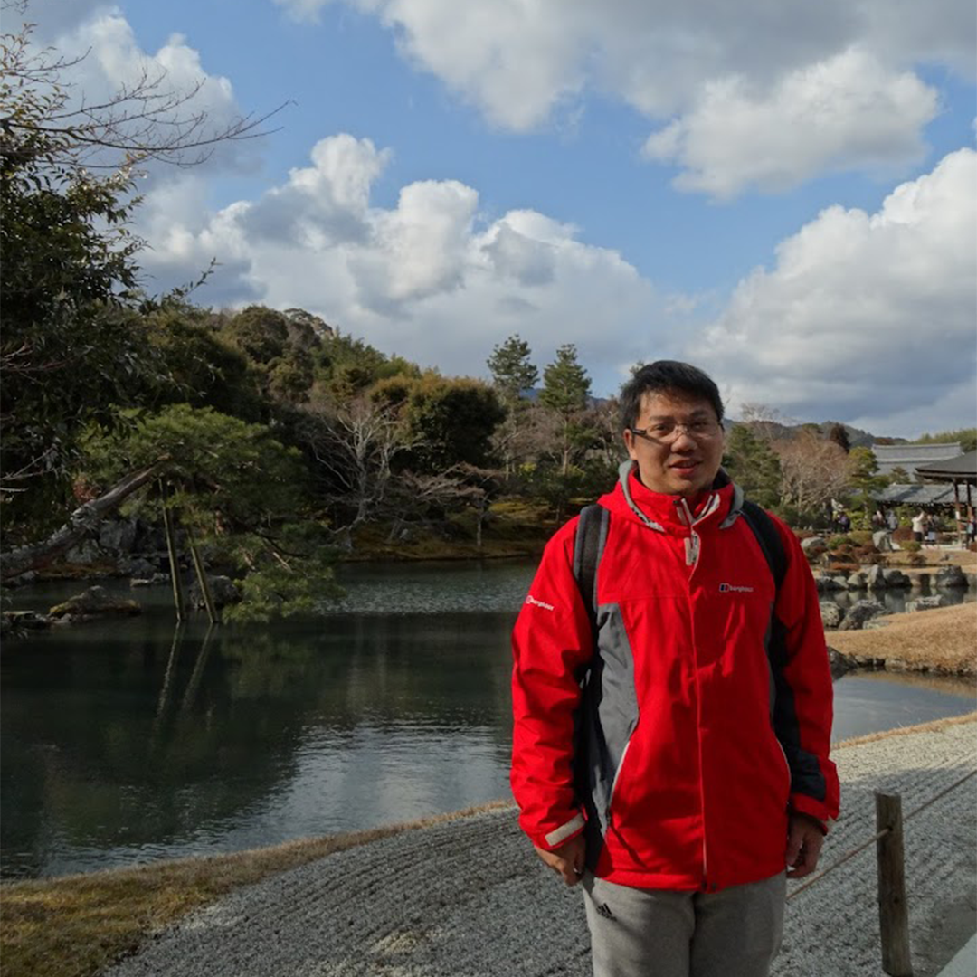 asian man with short black hair and glasses posing in front of a lake